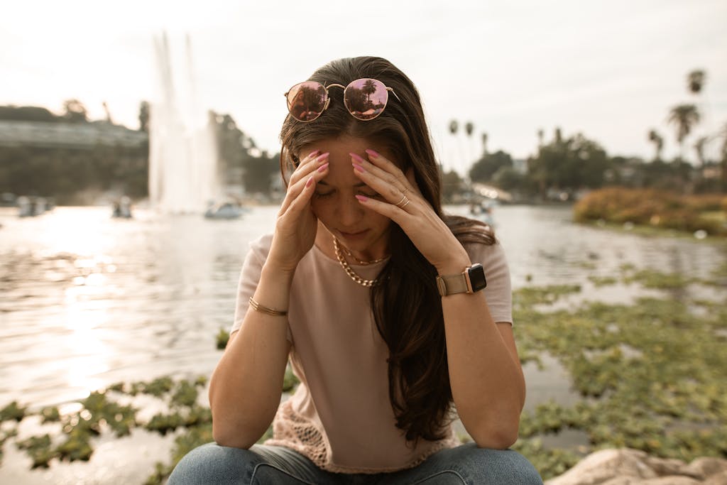 Distressed woman sitting on lakeside and touching face in despair